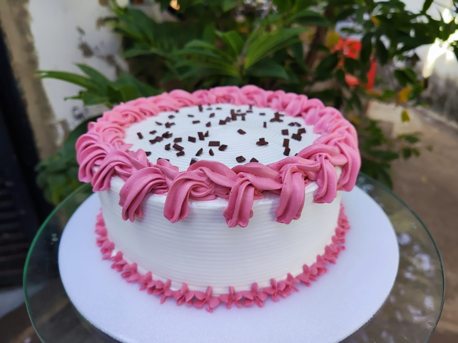 Bolo de festa com chantilly branco, bordas em rosa e granulado de chocolate